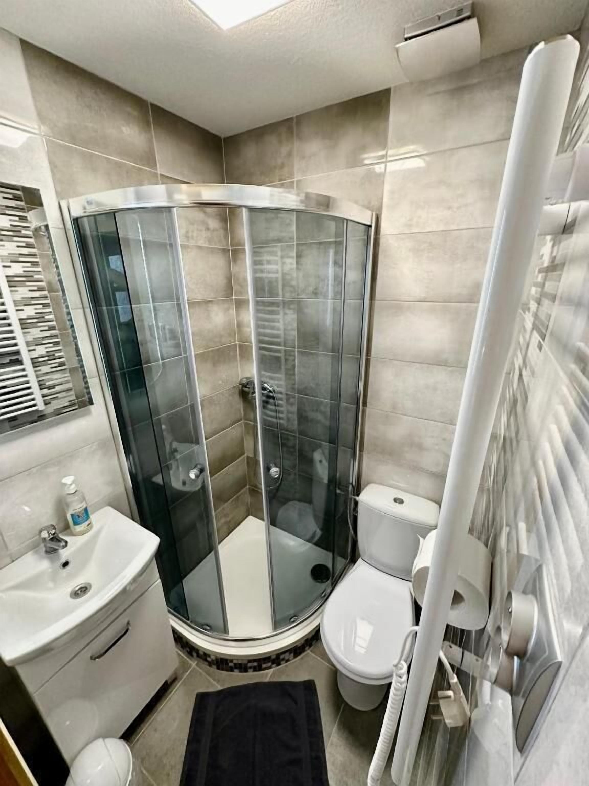 Et badeværelse med en glasvæg omkring brusebadet, en hvid vask og et toilet.