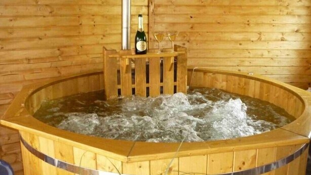 Un jacuzzi de madera con una botella y vasos sobre un pedestal de madera.