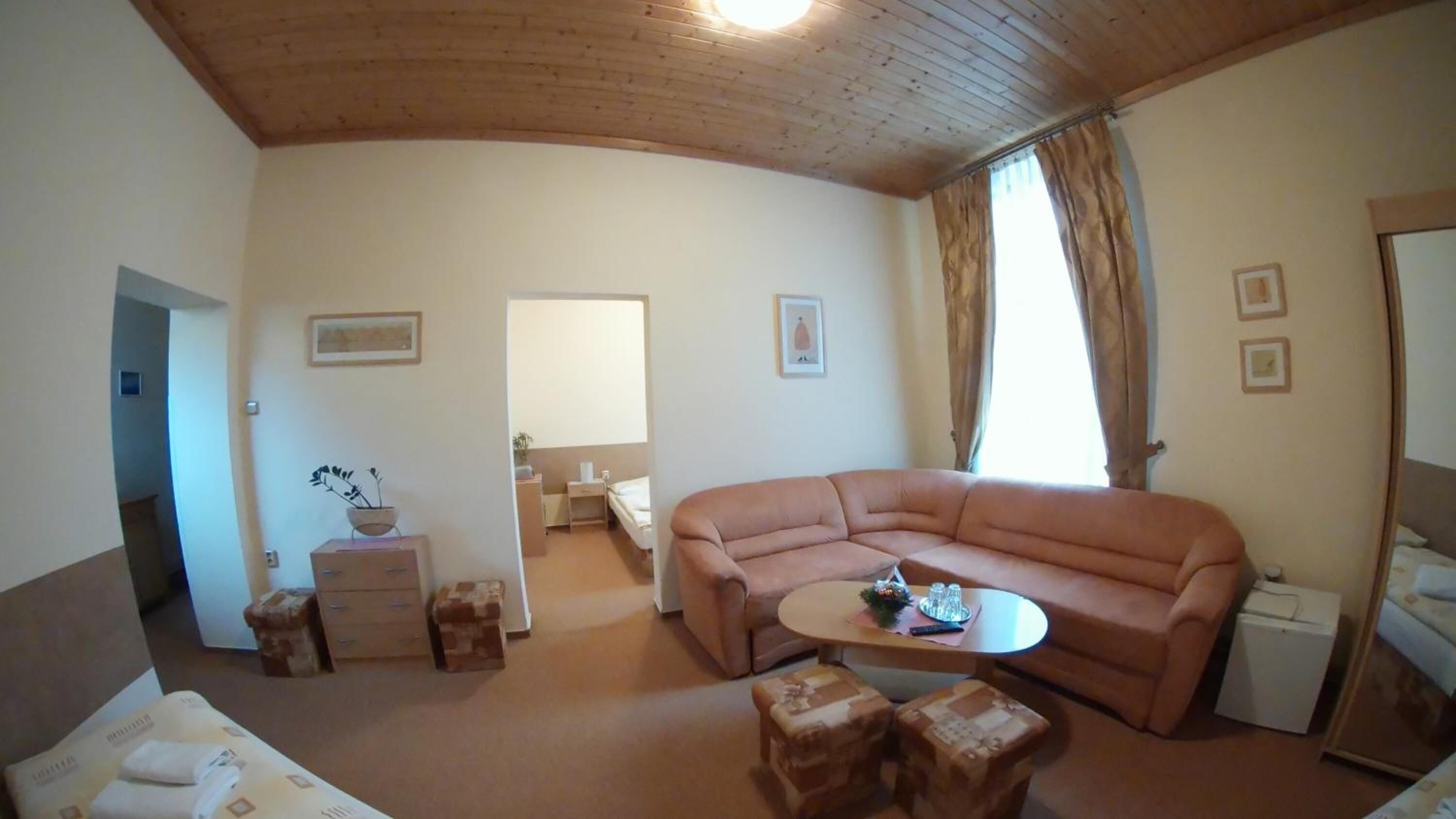 A cozy living room with a curved sofa, a small round table, and a coffee table. There is a door leading to a bathroom and a small cabinet with a plant.
