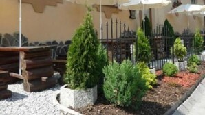 Un área de estar al aire libre con mesas y sombrillas, rodeada de arbustos decorativos y una cerca de metal.