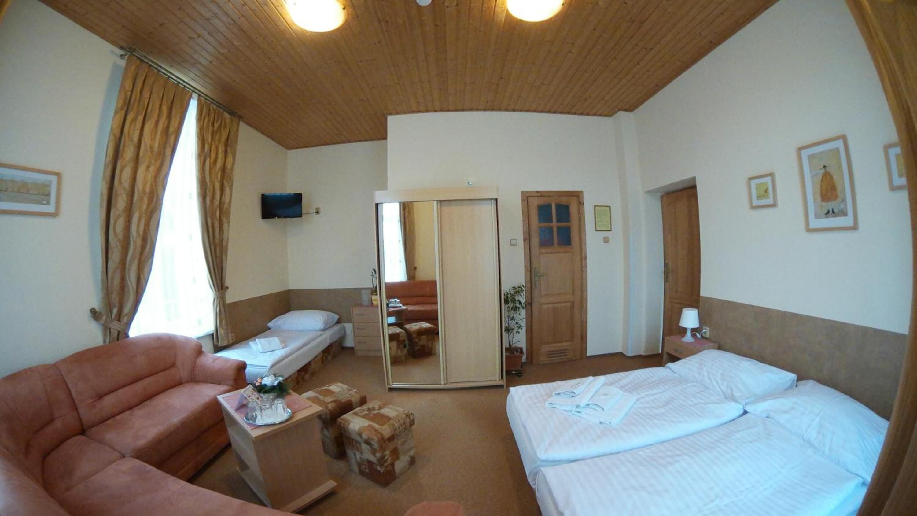 A hotel room with two beds, a sofa, a TV, and a mirror.