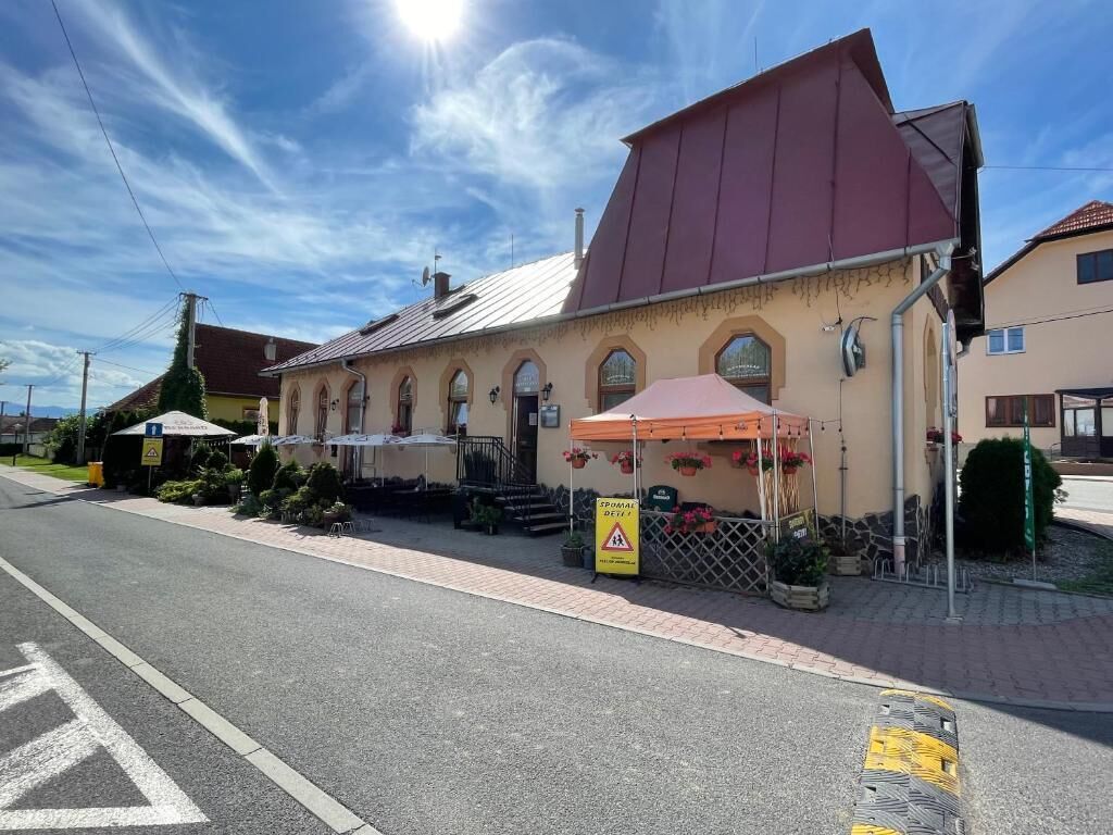 A building with a red roof, a covered outdoor seating area with umbrellas, and a sign indicating a restaurant.
