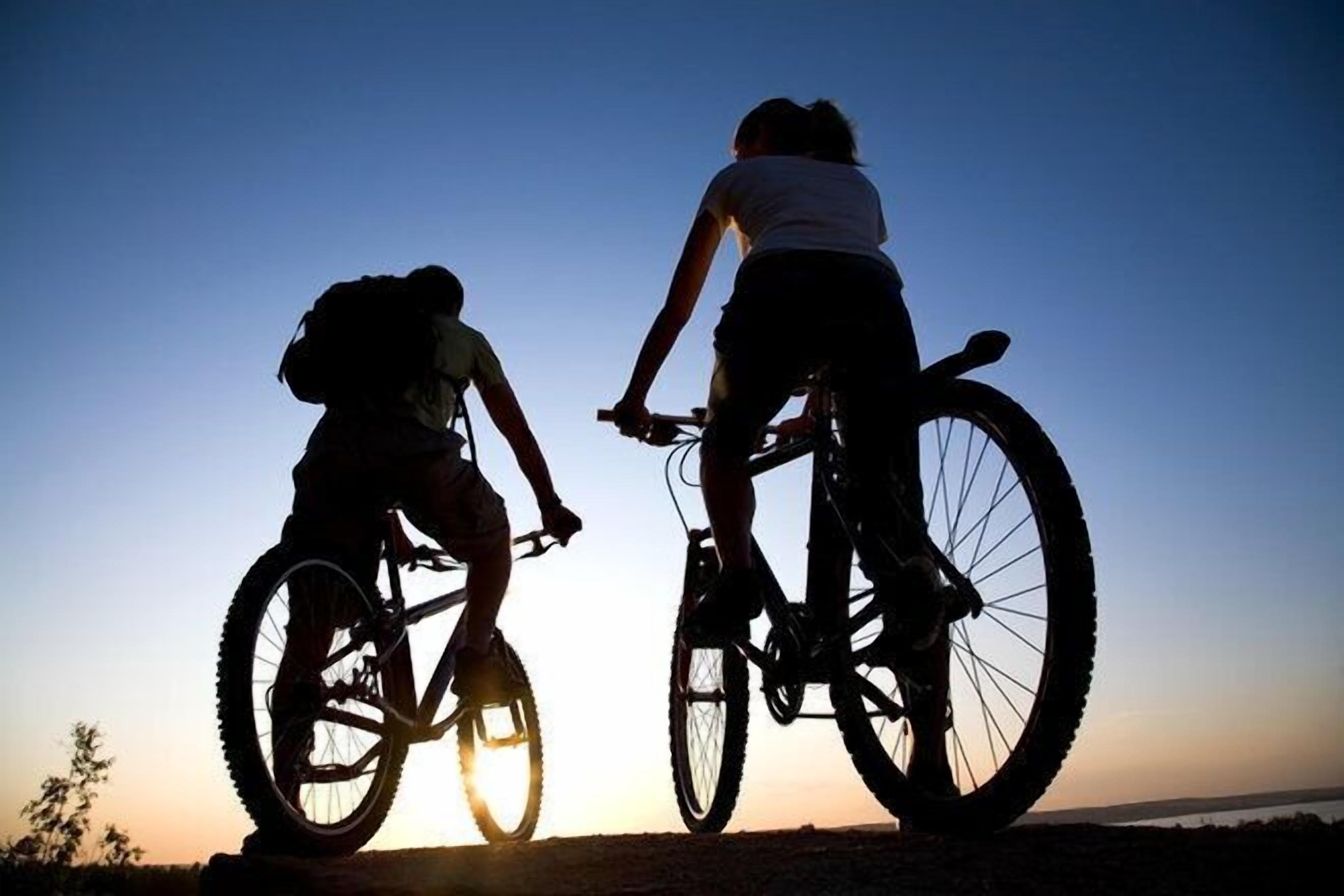 Deux cyclistes se détachent sur le ciel au coucher du soleil.