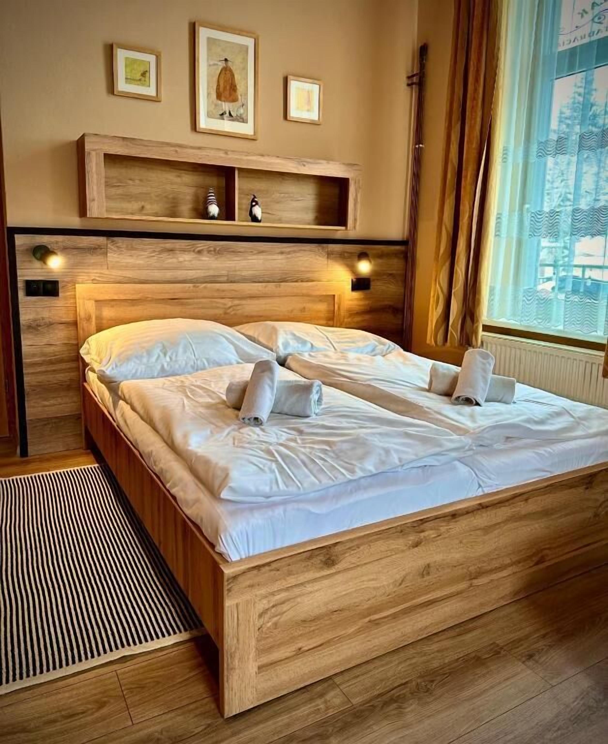 A double bed with a wooden headboard, two wall-mounted lamps, and a window with curtains.