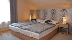 Un dormitorio con techo de madera, una cama con ropa de cama de estampado geométrico, dos lámparas de noche y una pared con motivo de hojas de cebra.