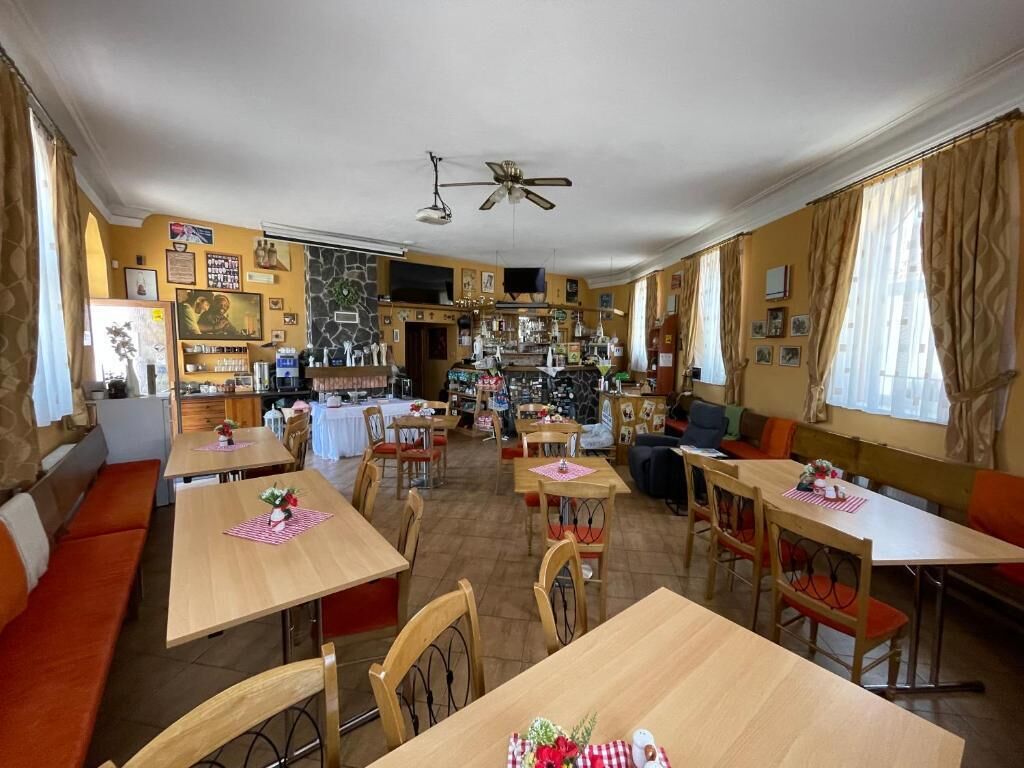 Un comedor con varias mesas y sillas, una zona de bar al fondo, y una cocina visible a través de un vano abierto.