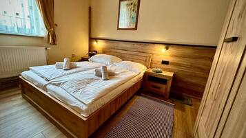 Una habitación de hotel con una cama de madera, una mesita de noche, un cuadro enmarcado en la pared y una ventana con cortinas.