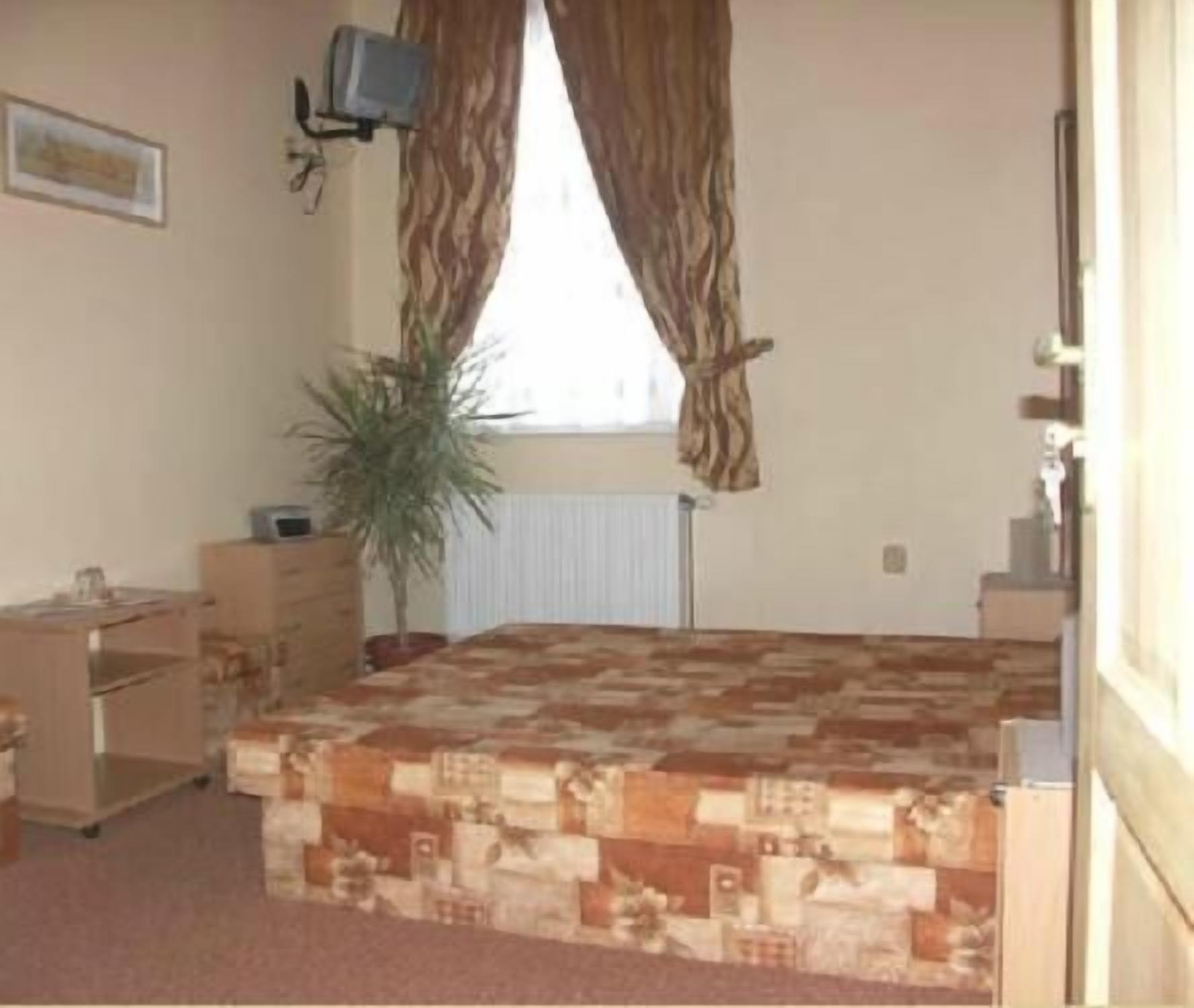 A bedroom with a bed, a desk, a chair, a radiator, and a window with curtains.