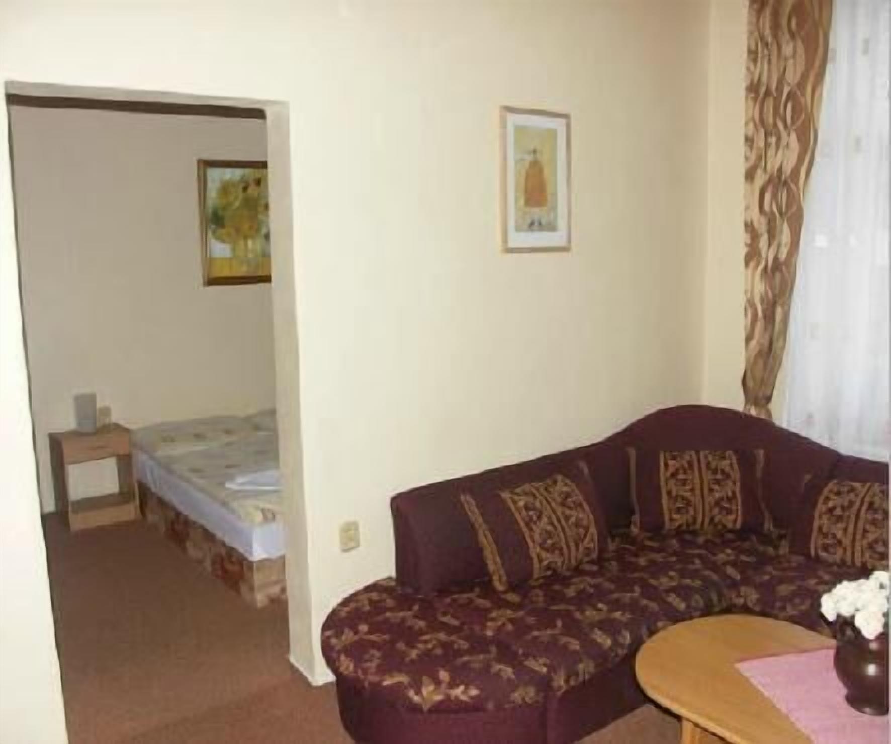 Una habitación con una cama, un sofá y una mesita. Hay un cuadro en la pared y una cortina en la ventana.