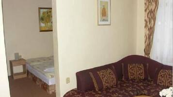 Una habitación con una cama, un sofá y una mesita. Hay un cuadro en la pared y una cortina en la ventana.