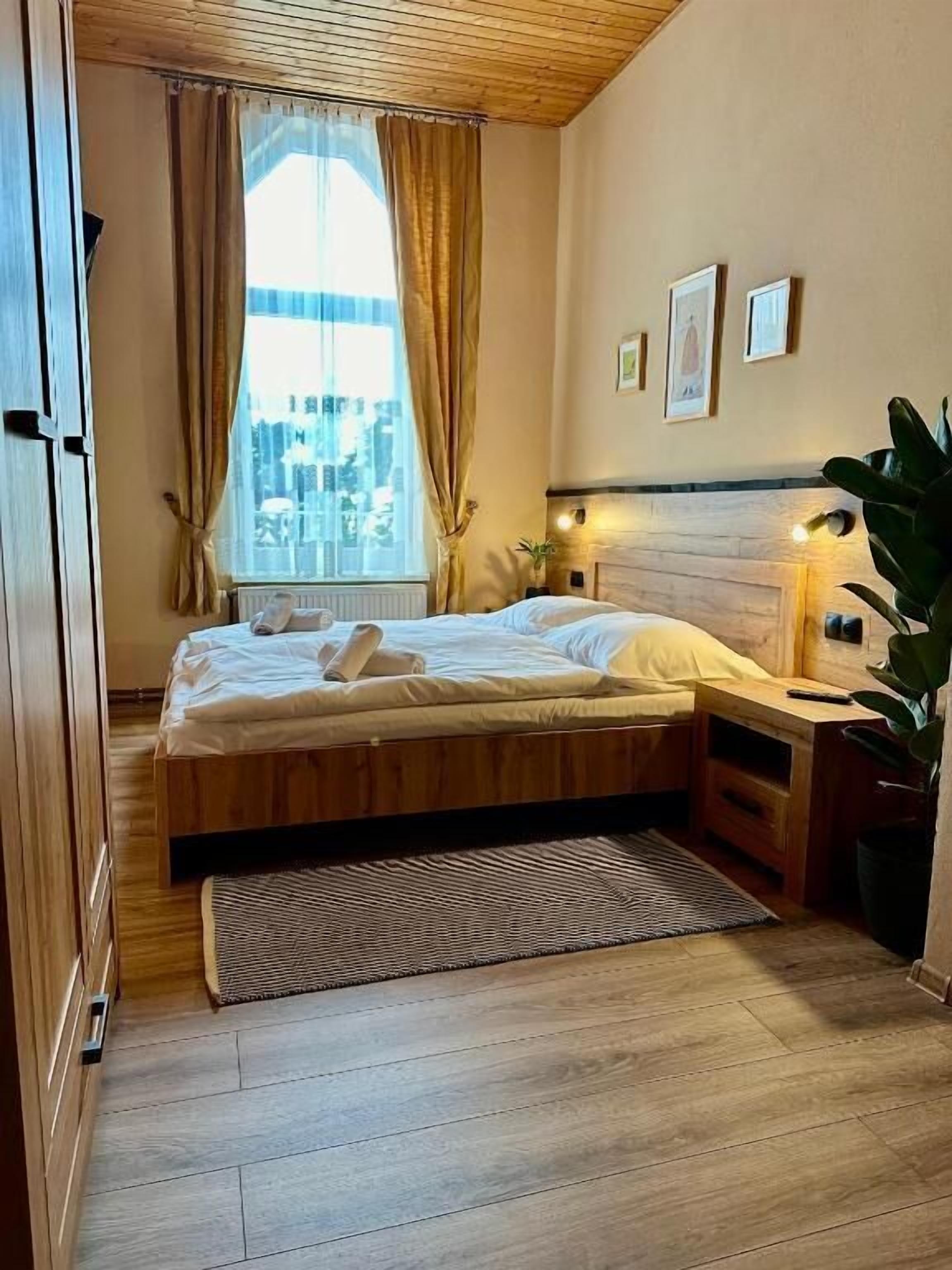 A bedroom with a bed, a bedside table, a window with curtains, and a view of the city.