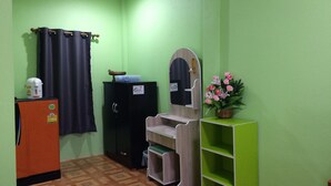 A room with green walls, a wooden floor, a black cabinet, a small orange refrigerator, a mirror with a wooden frame, and a green shelf with a plant. - Ban Khun Mor (Phrao)