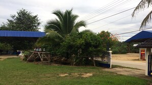 A grassy area with a palm tree, a wooden structure, and a blue-roofed building. - Ban Khun Mor (Phrao)