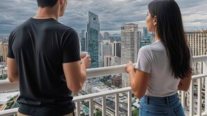 Twee personen staan op een balkon met uitzicht op een stadslandschap met moderne gebouwen.