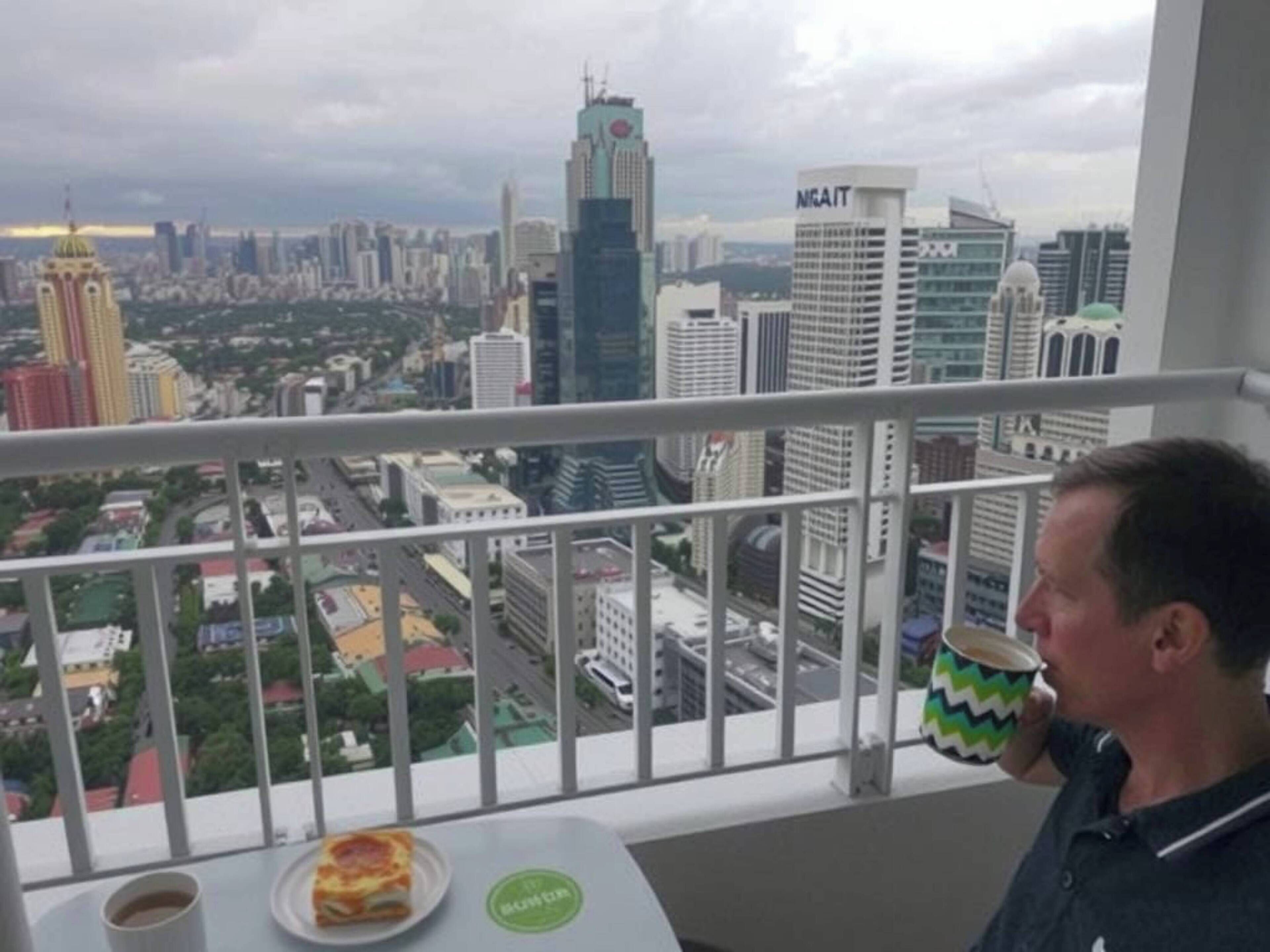 A man on a balcony with a city view, a plate of food, and a cup.
