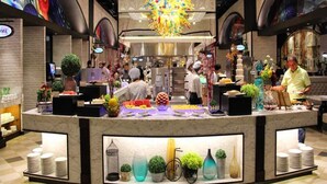 Een moderne hotel lobby met een centraal receptiebalie, decoratieve vazen en een kleurrijke kroonluchter.