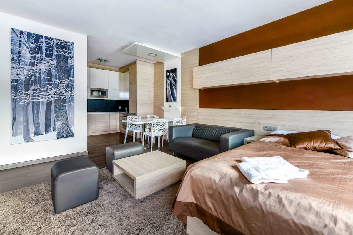 A modern hotel room with a large bed, a sofa, a dining table with chairs, and artwork on the walls.