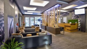 A modern reception area with a wooden reception desk, a comfortable seating area with sofas, and a large window providing natural light. - Hotel Pecr Well (Pec pod Snezkou)