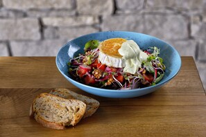 Un tazón de ensalada con una rebanada de pan sobre una mesa de madera.