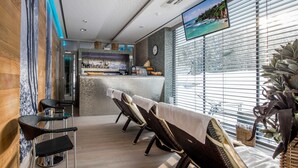 A modern bar area with a counter, bar stools, and a television screen displaying a scenic view. - Hotel Pecr Well (Pec pod Snezkou)