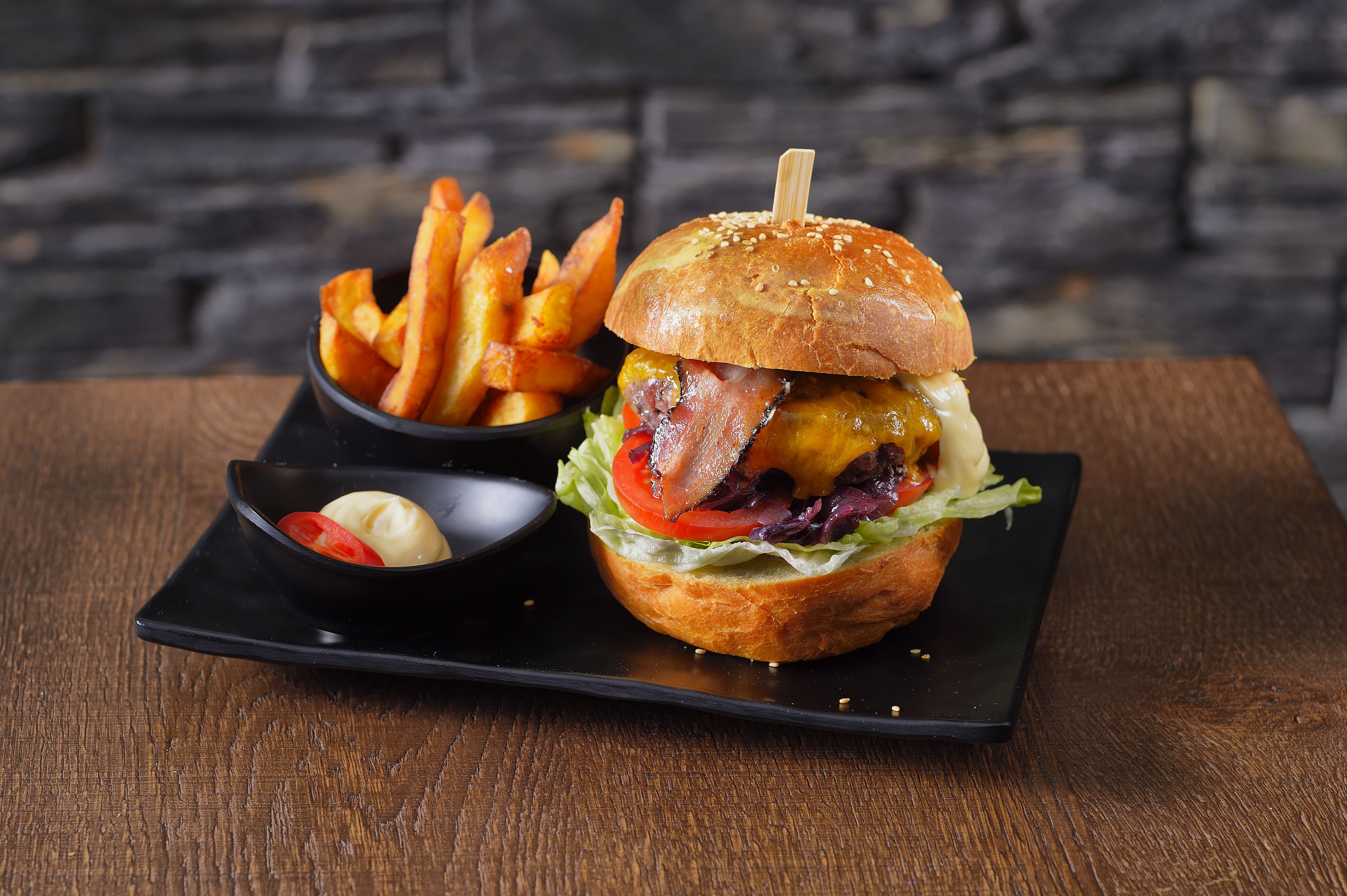 A burger with fries and a small bowl of sauce on a black plate.