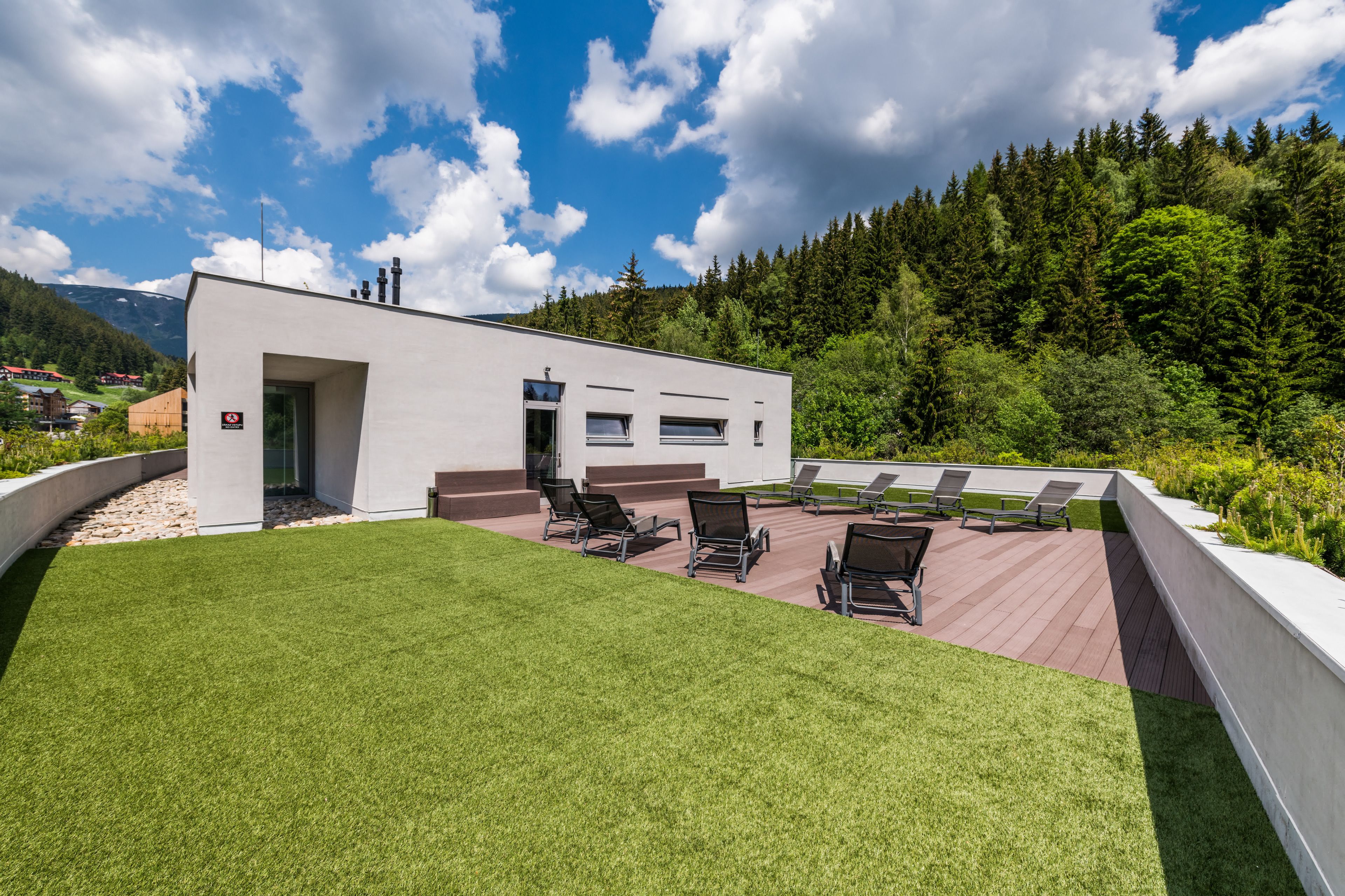 A modern building with a patio area featuring outdoor seating and a view of a forested mountain range.