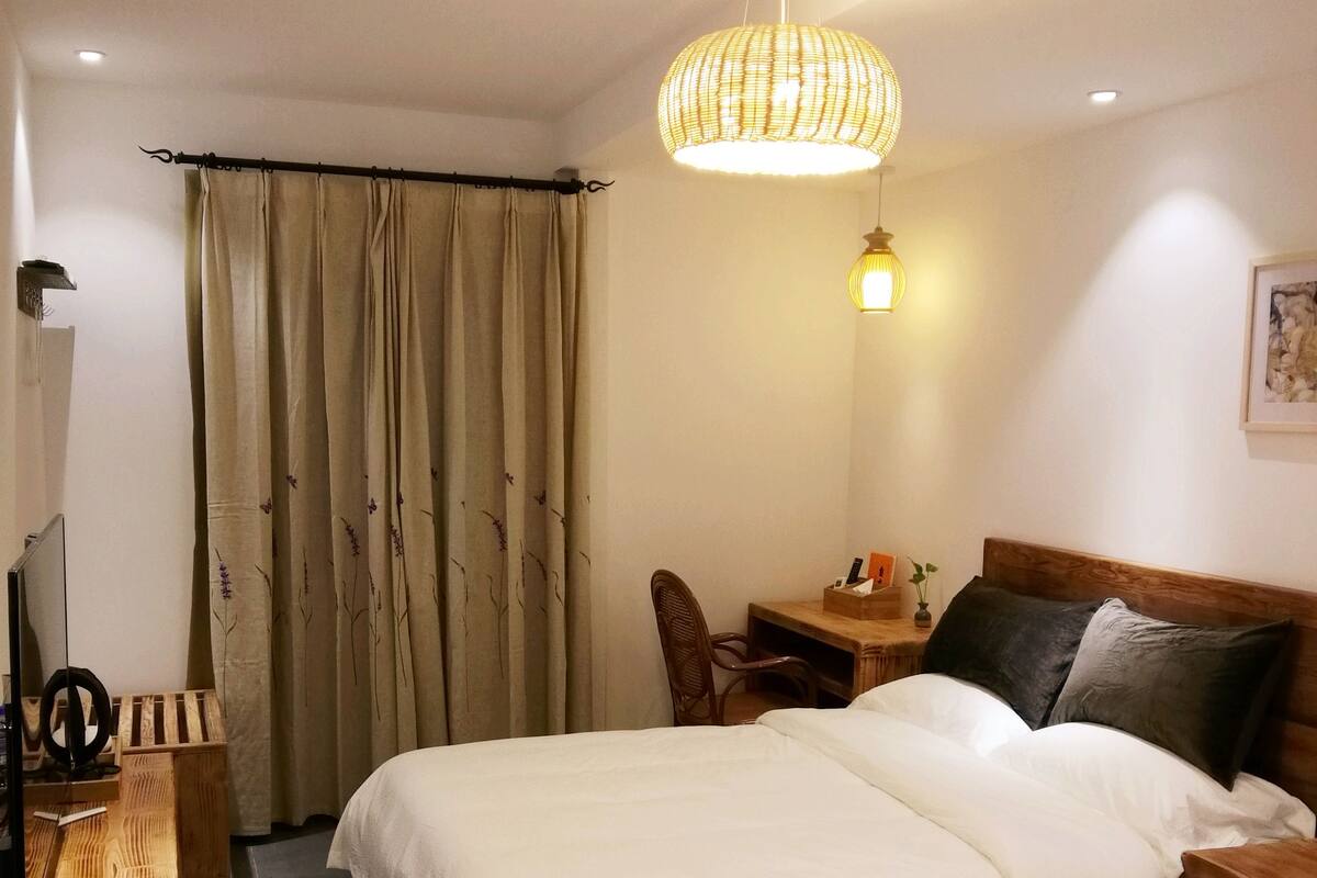 Quarto de hotel com duas camas, uma escrivaninha, uma cadeira, uma televisão e uma luminária no teto.