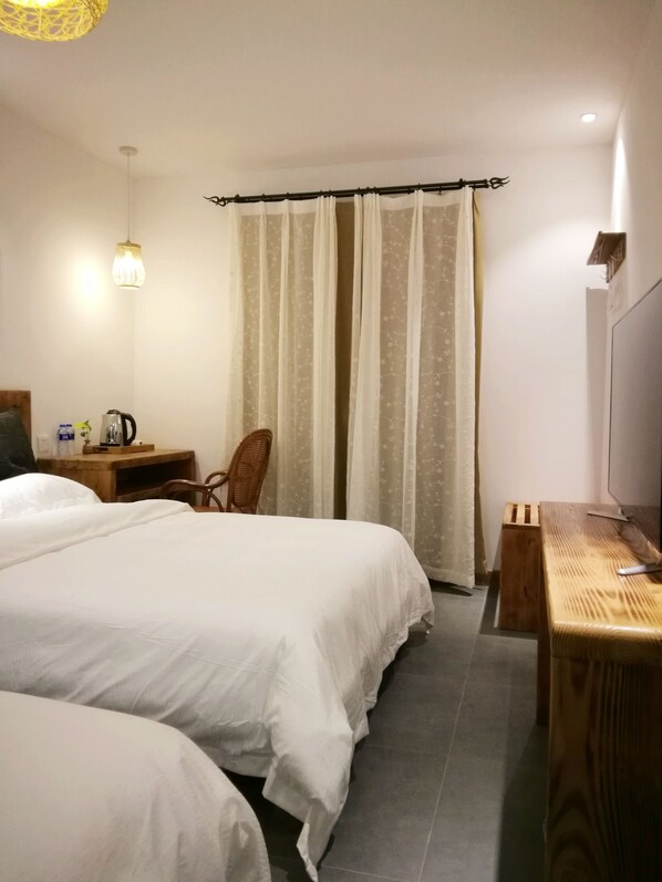 Habitación de hotel con dos camas, un escritorio de madera, una silla, un televisor y una ventana con cortinas.