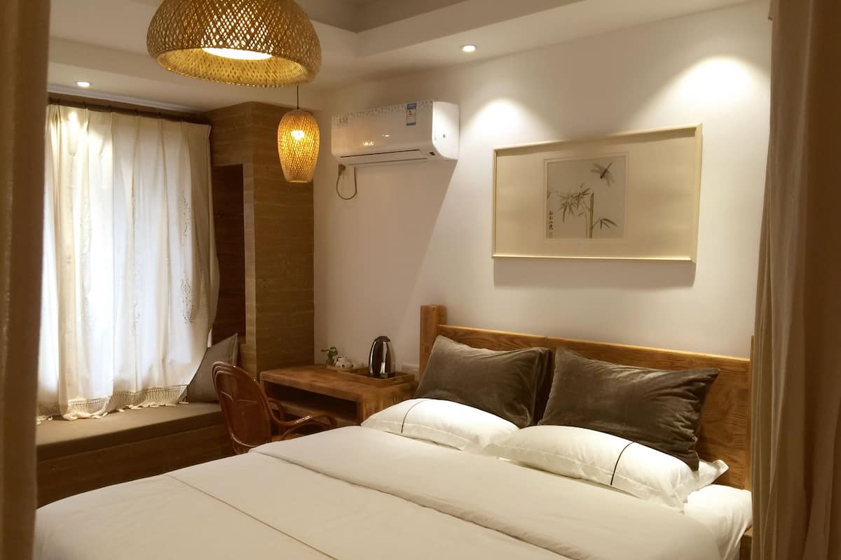 Quarto de hotel bem arrumado com uma cama grande, uma escrivaninha de madeira, uma cadeira e um candeeiro pendente.