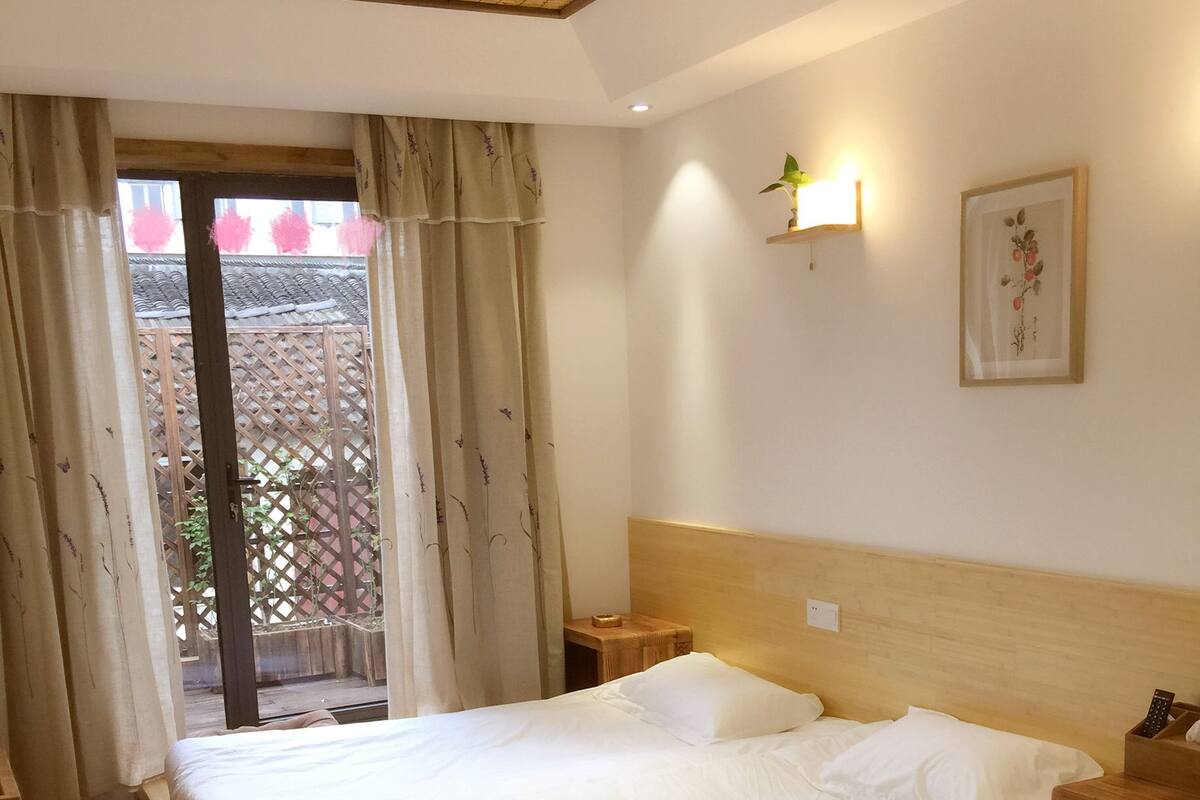 Quarto de hotel com duas camas, cabeceira de madeira, mesa de cabeceira pequena e janela com cortinas.