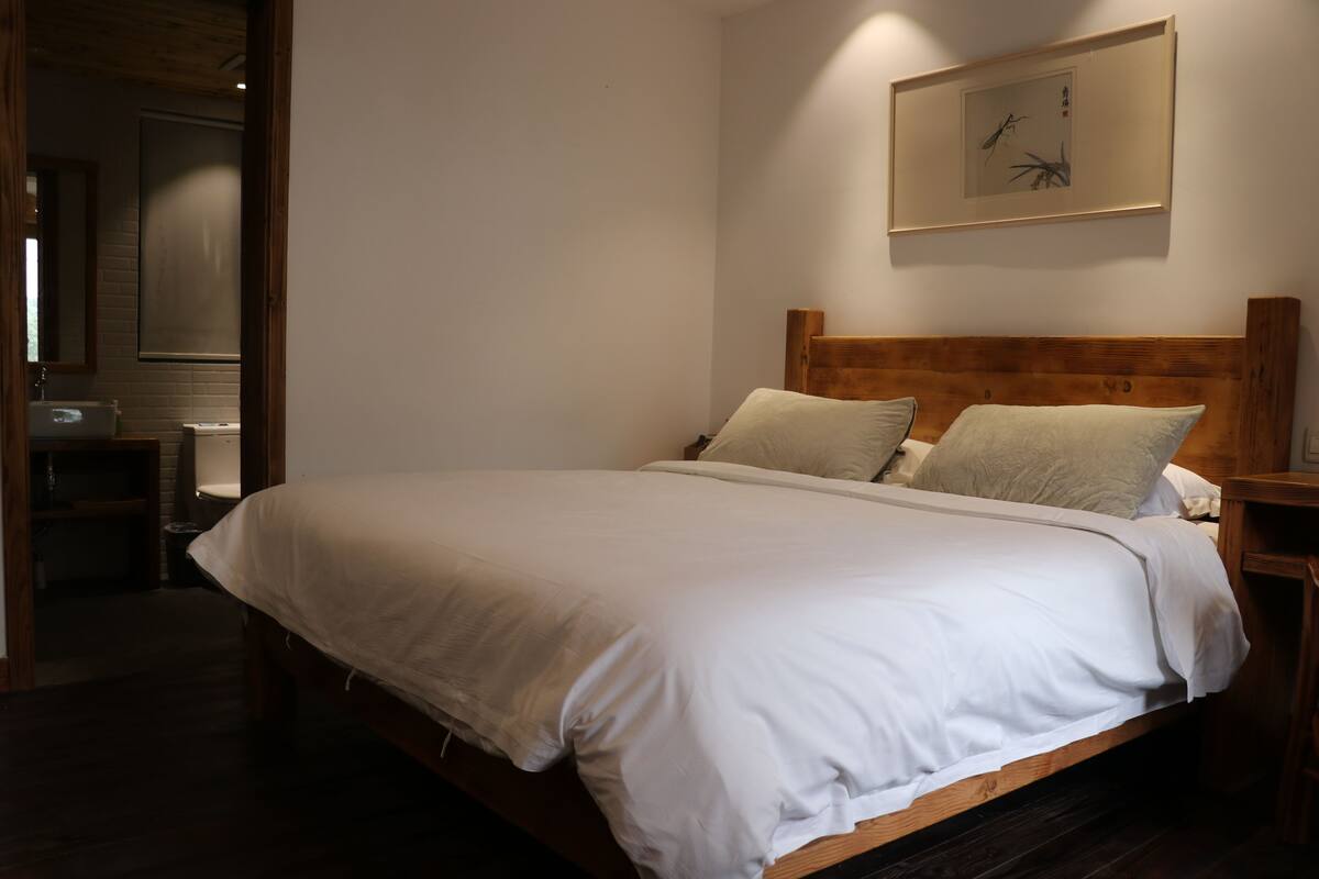 Cama bem arrumada com lençóis brancos, cabeceira de madeira e uma obra de arte emoldurada acima.