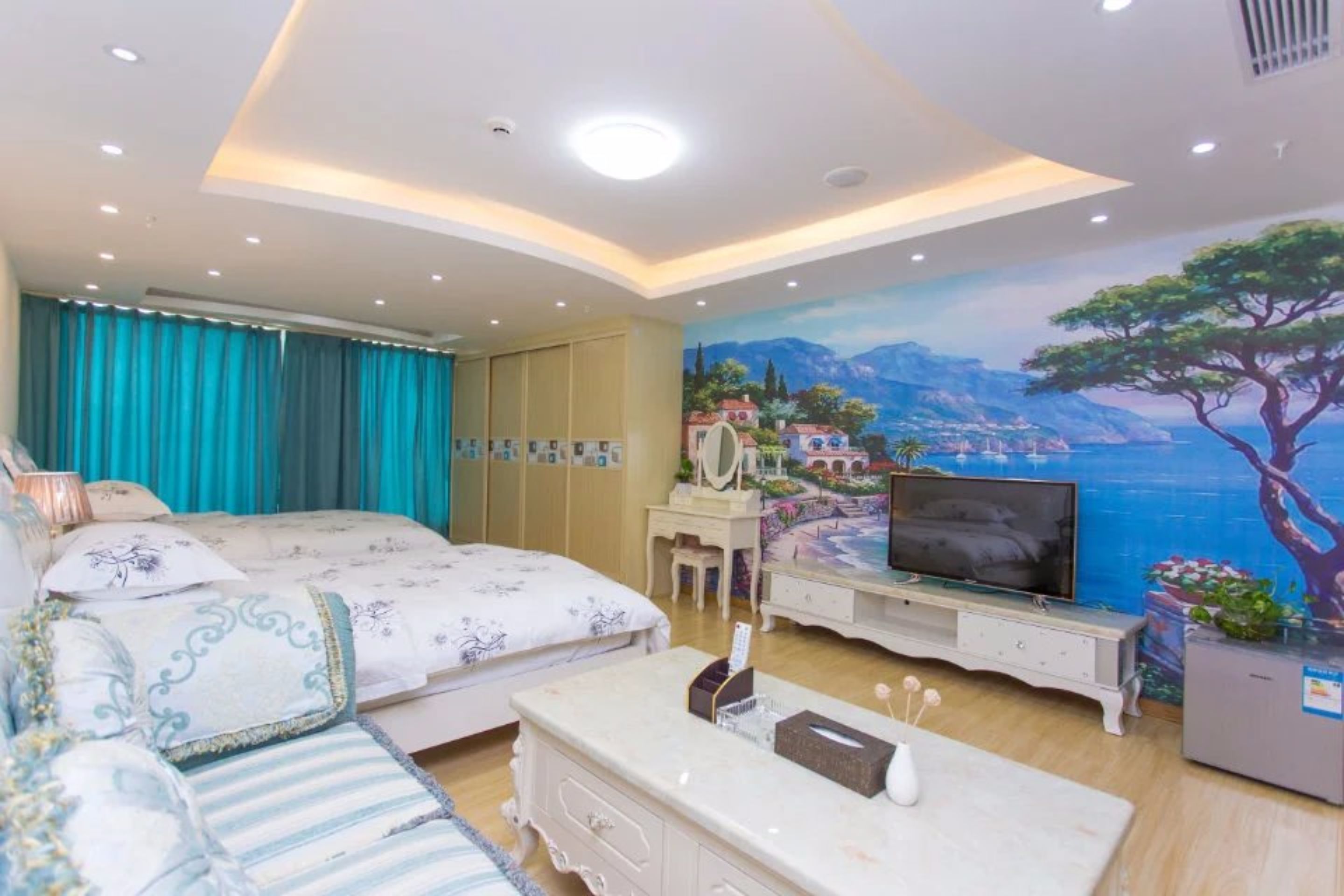 Un dormitorio con cama, televisor, cómoda y un mural de un paisaje costero.