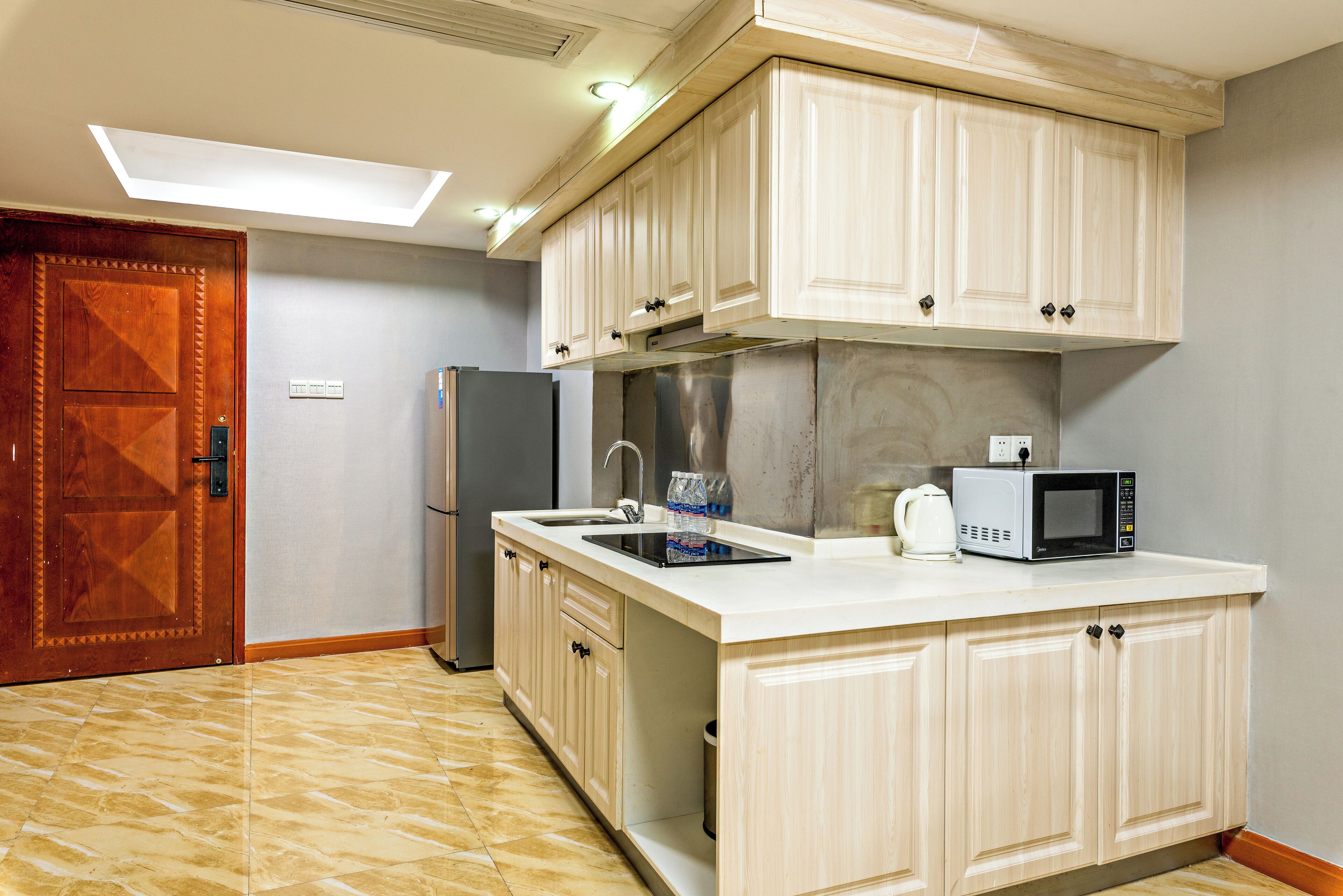 A kitchen with light wooden cabinets, a stainless steel range hood, a microwave, and a refrigerator.