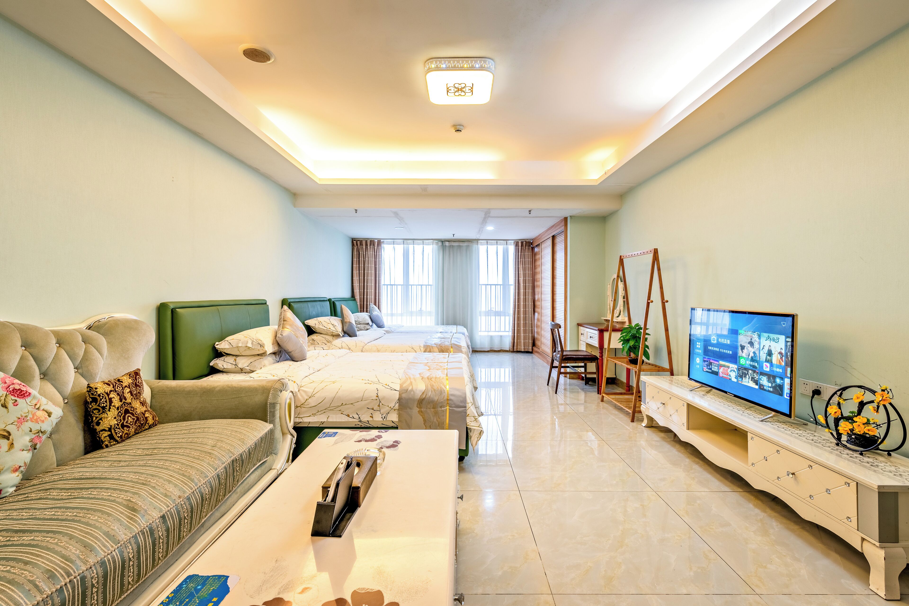 Ein helles Hotelzimmer mit einer Couch, zwei Betten, einem Fernseher und einem Schreibtisch mit Stuhl.
