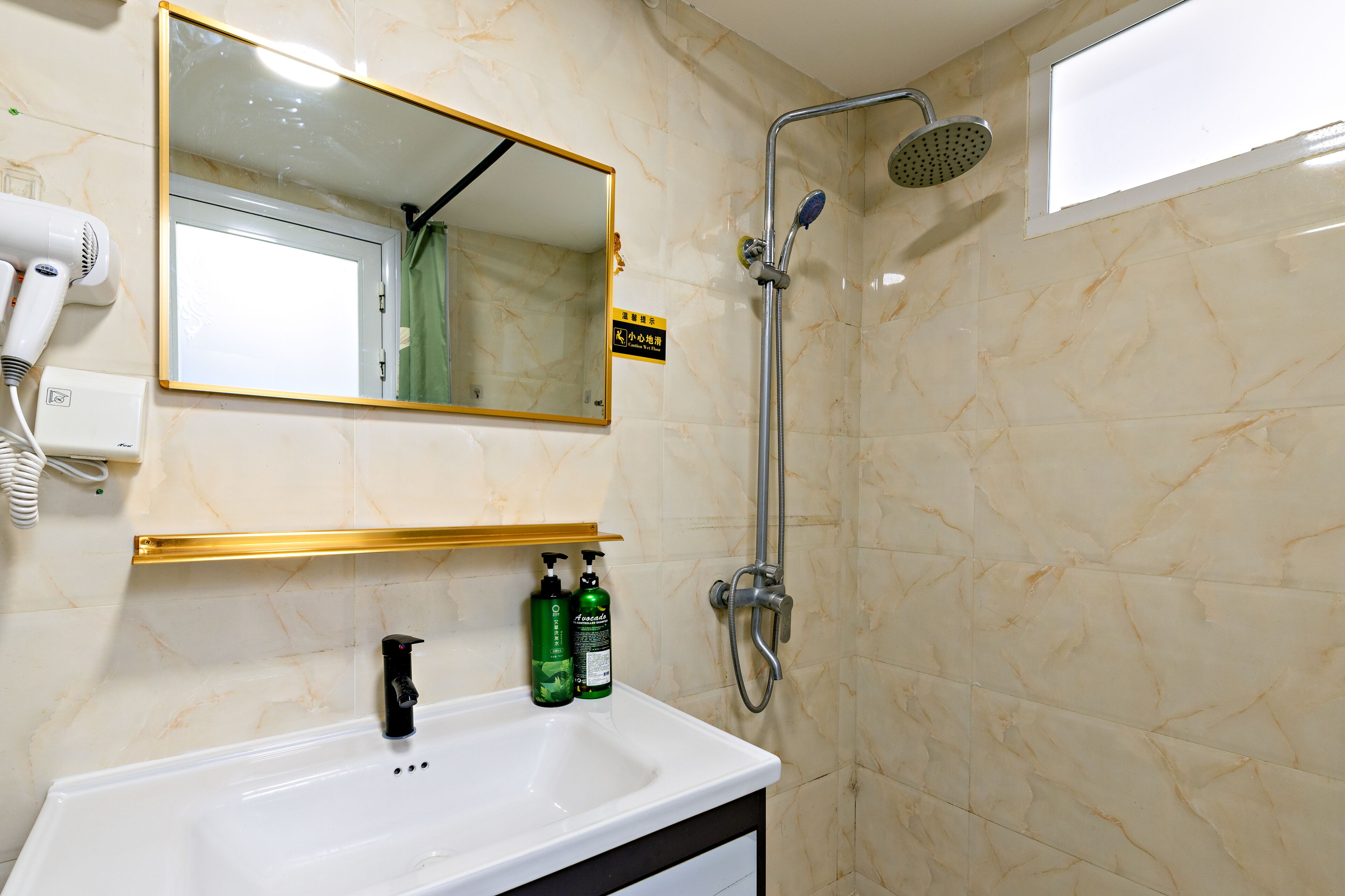 A bathroom with a white sink, a mirror, a handheld showerhead, and two bottles of shampoo.