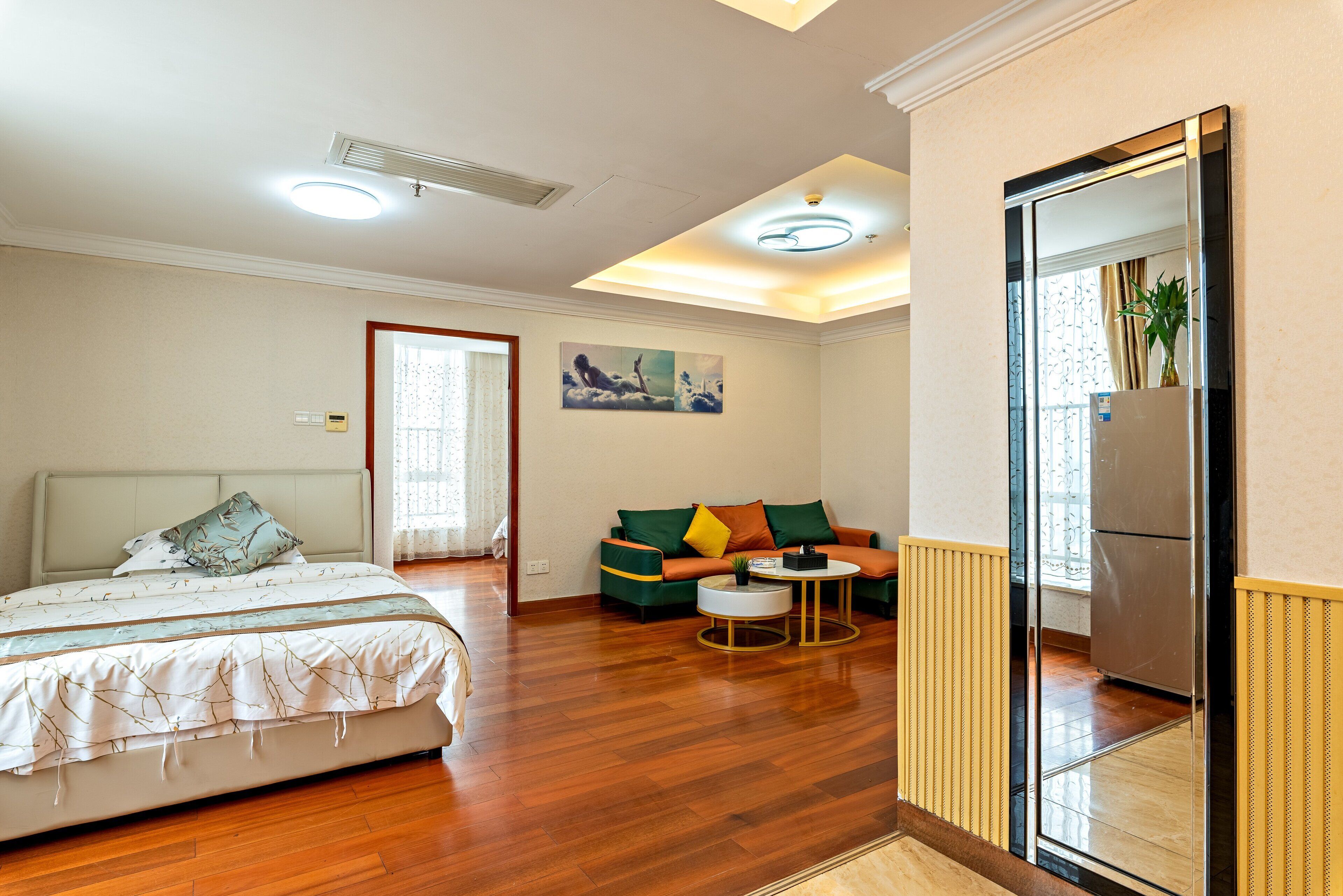 A bedroom with a bed, a sofa, a small round table, and a mirror.