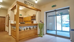 Un mostrador de recepción con estructura de madera, un área de recepción y una puerta de cristal que da al exterior.