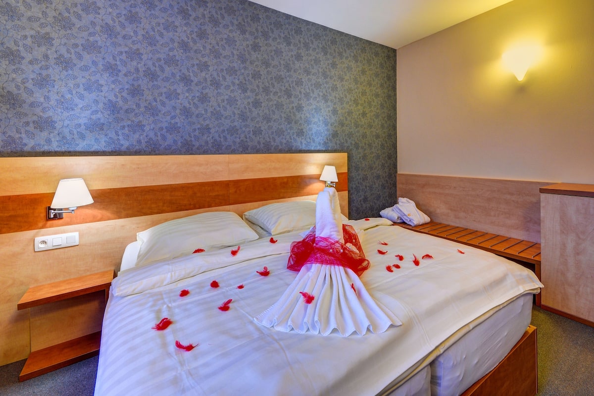 A hotel room with a large bed, two bedside tables with lamps, a wooden headboard, and a wall-mounted light fixture.