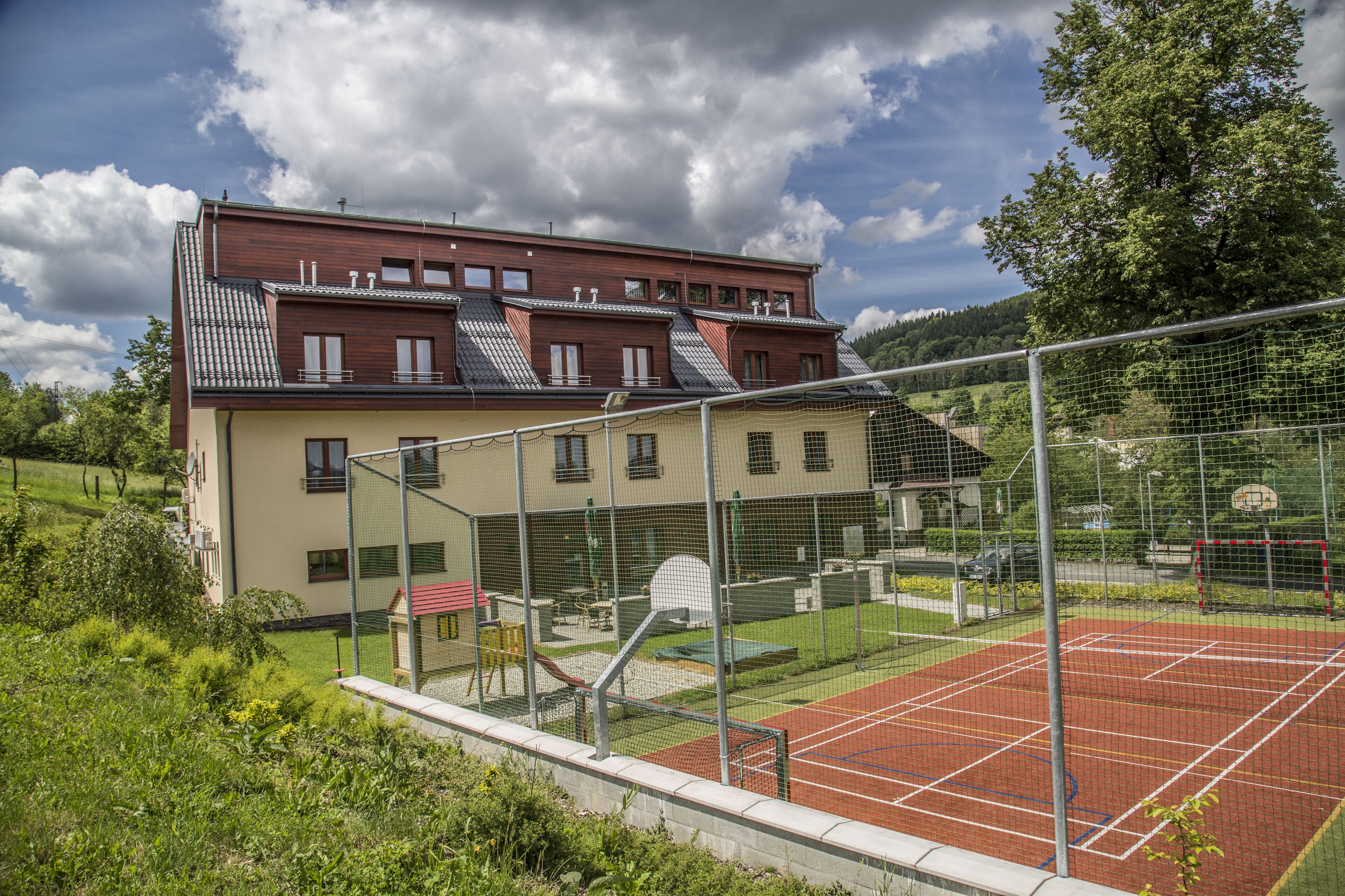 Edificio residencial con cancha de tenis, rodeado por una valla y follaje.
