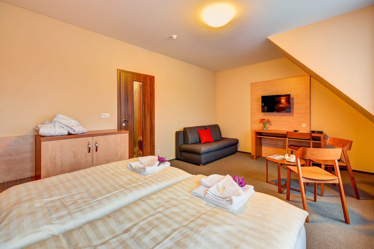 A hotel room with two beds, a desk, a chair, a sofa, and a television.