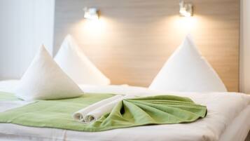 A neatly made bed with white pillows and a green towel, a wooden headboard, and two wall-mounted lights.