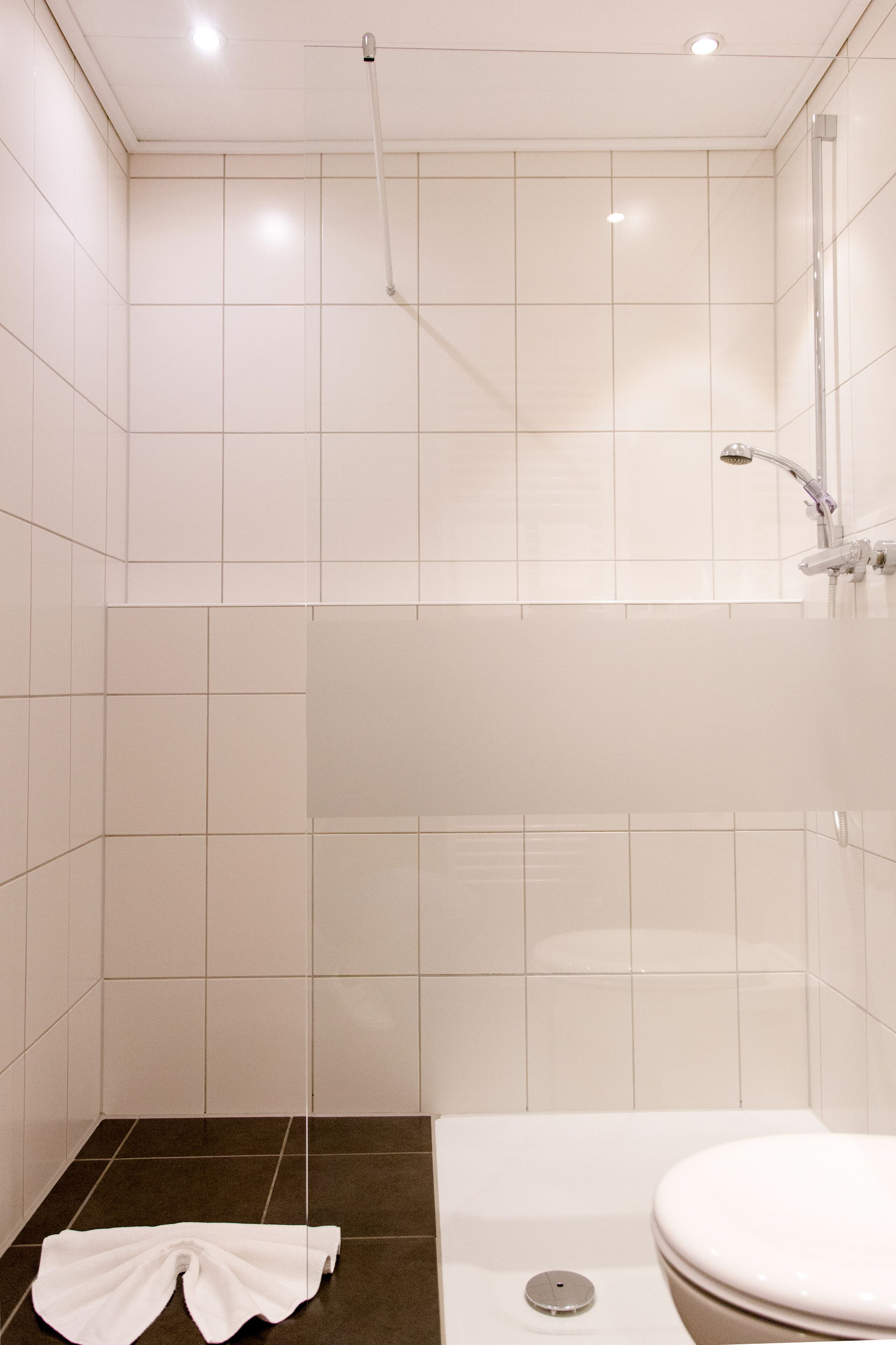 Ein modernes Badezimmer mit weißen Fliesen, einer Badewanne, einer Toilette und einer Dusche.
