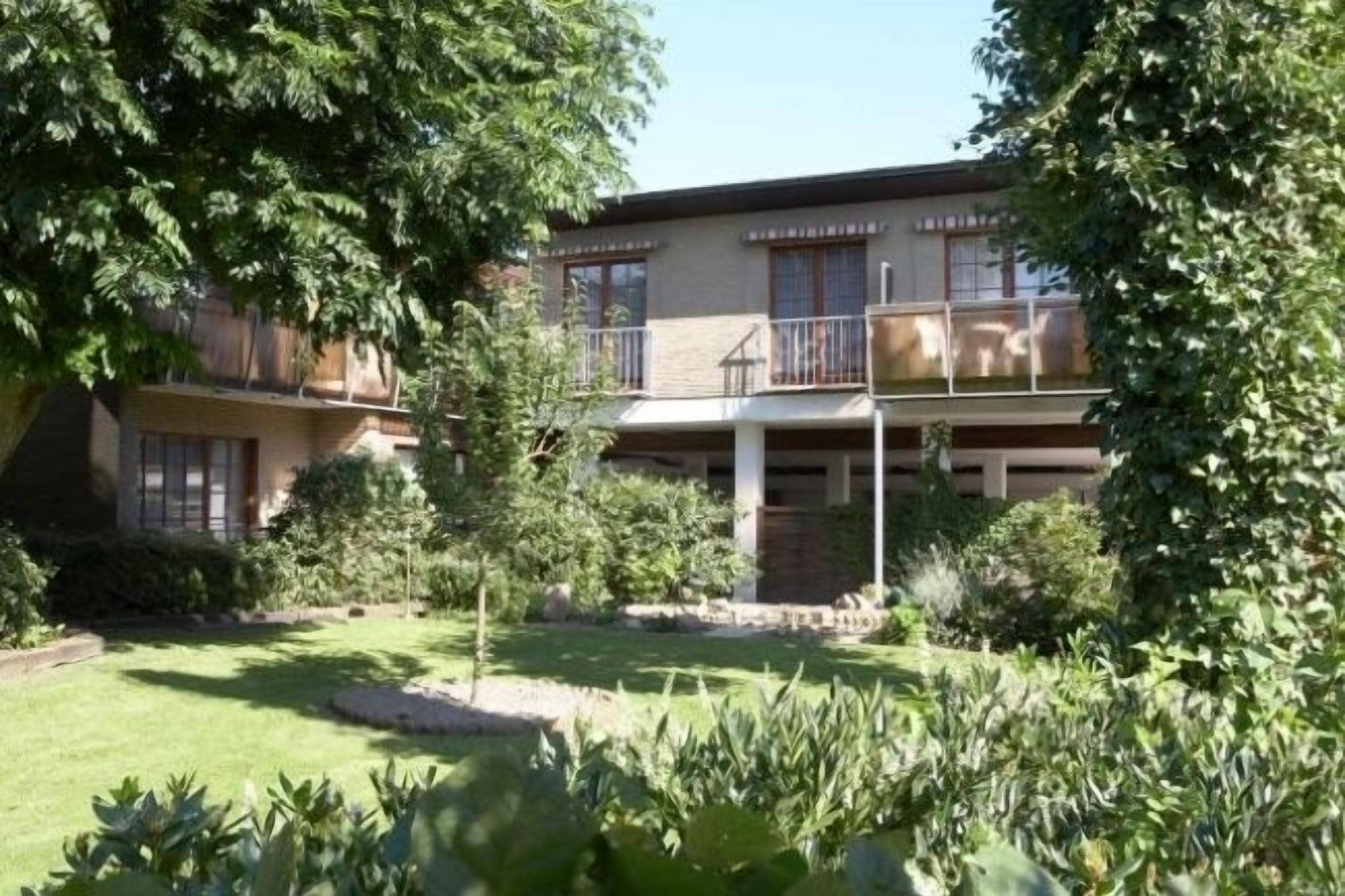 A two-story building with a balcony on the upper floor, surrounded by lush greenery and a well-maintained lawn.