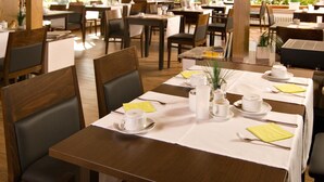 Un restaurante con varias mesas dispuestas para comer, con manteles blancos, cubiertos ordenados y un jarrón central con follaje.