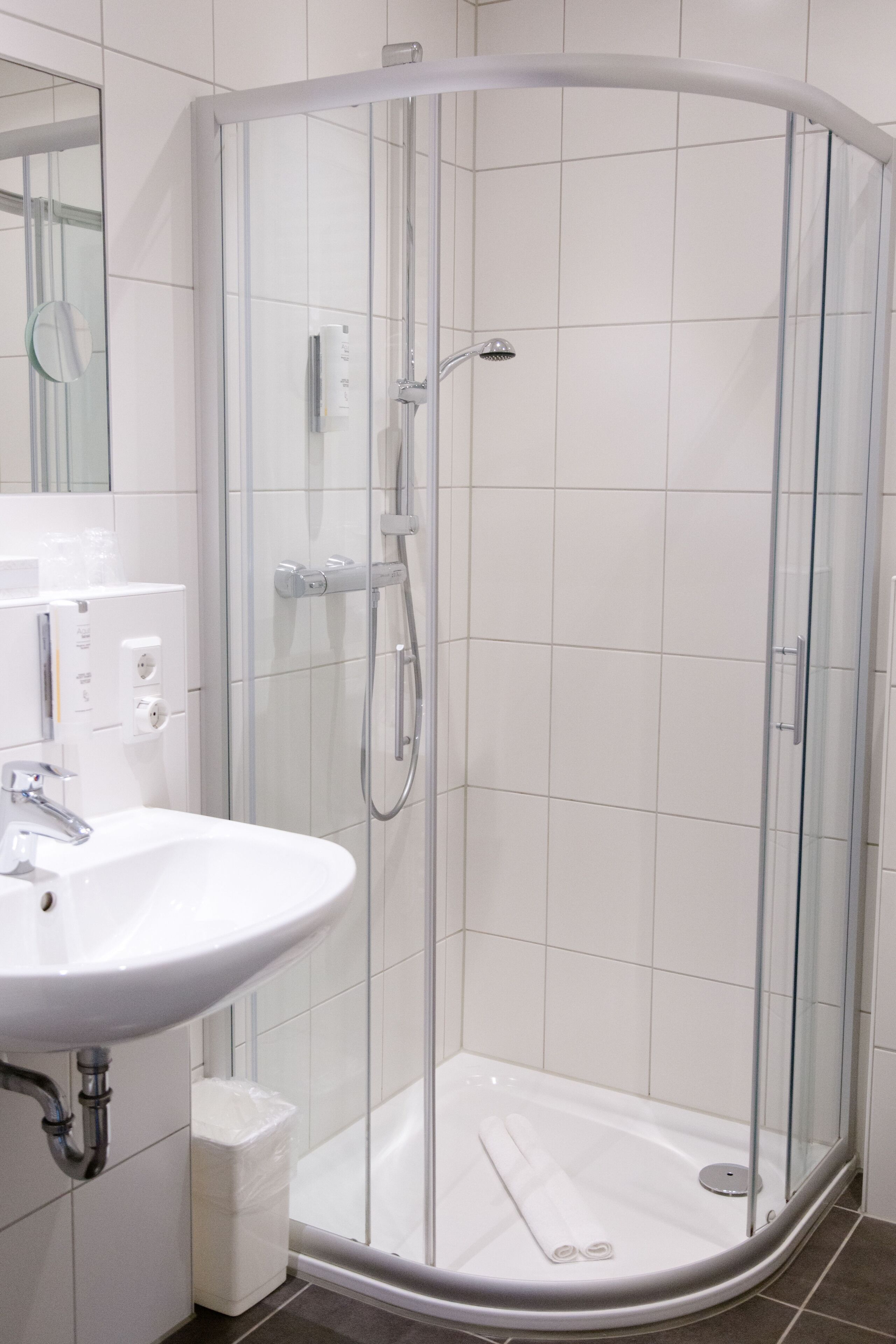 A modern bathroom with a glass-enclosed shower, a white sink, and a mirror.