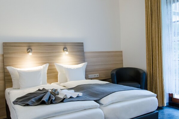 A hotel room with a bed, two bedside lamps, a chair, and a window with curtains.