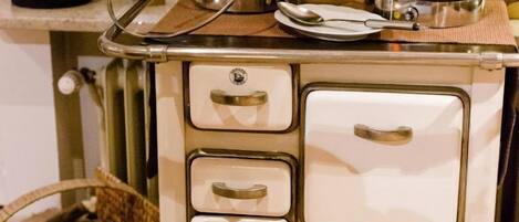 Una kitchenette antigua con estufa, ollas y una cesta de leña.