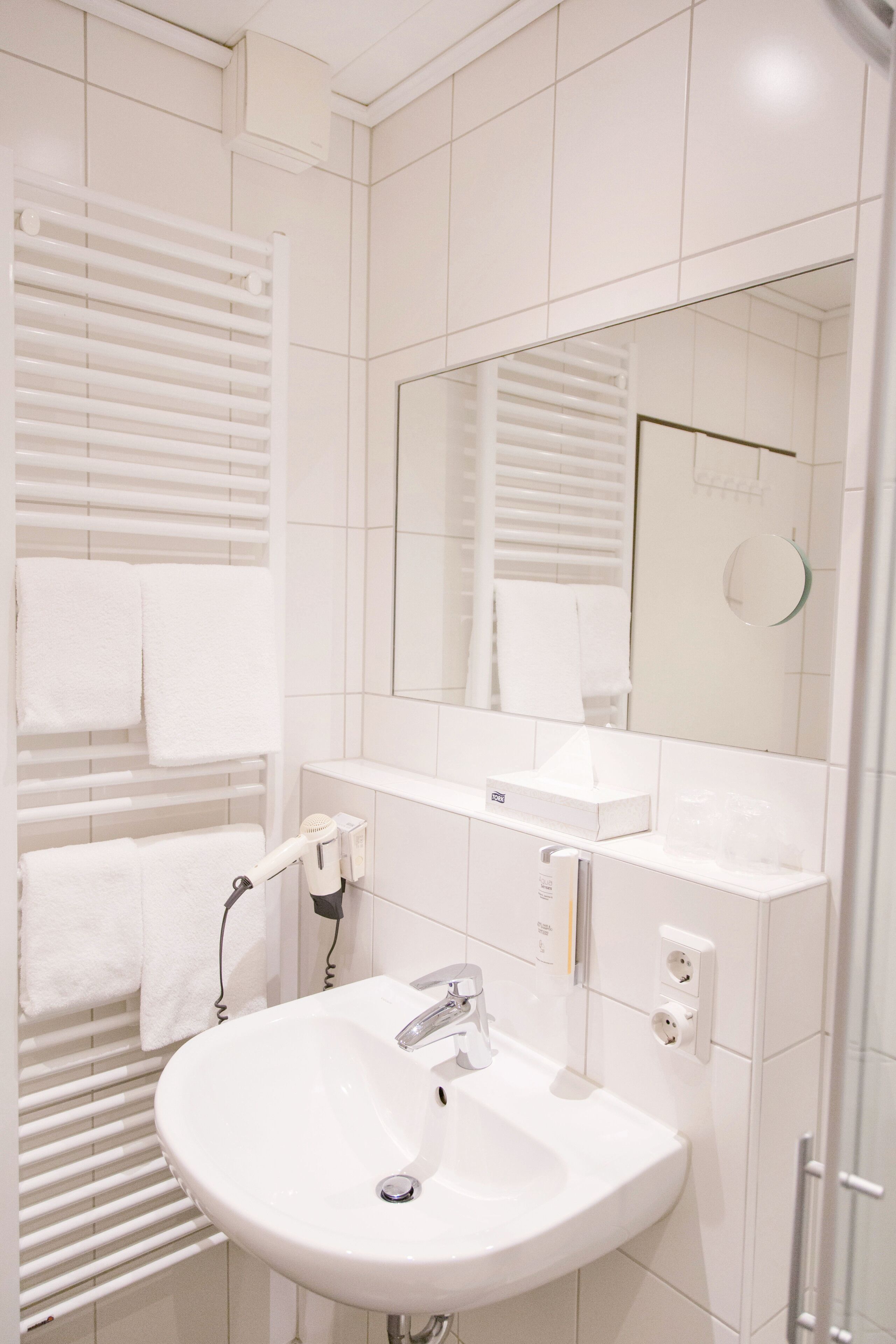 Un baño moderno con lavabo blanco, espejo, toallero y cabina de ducha de vidrio.