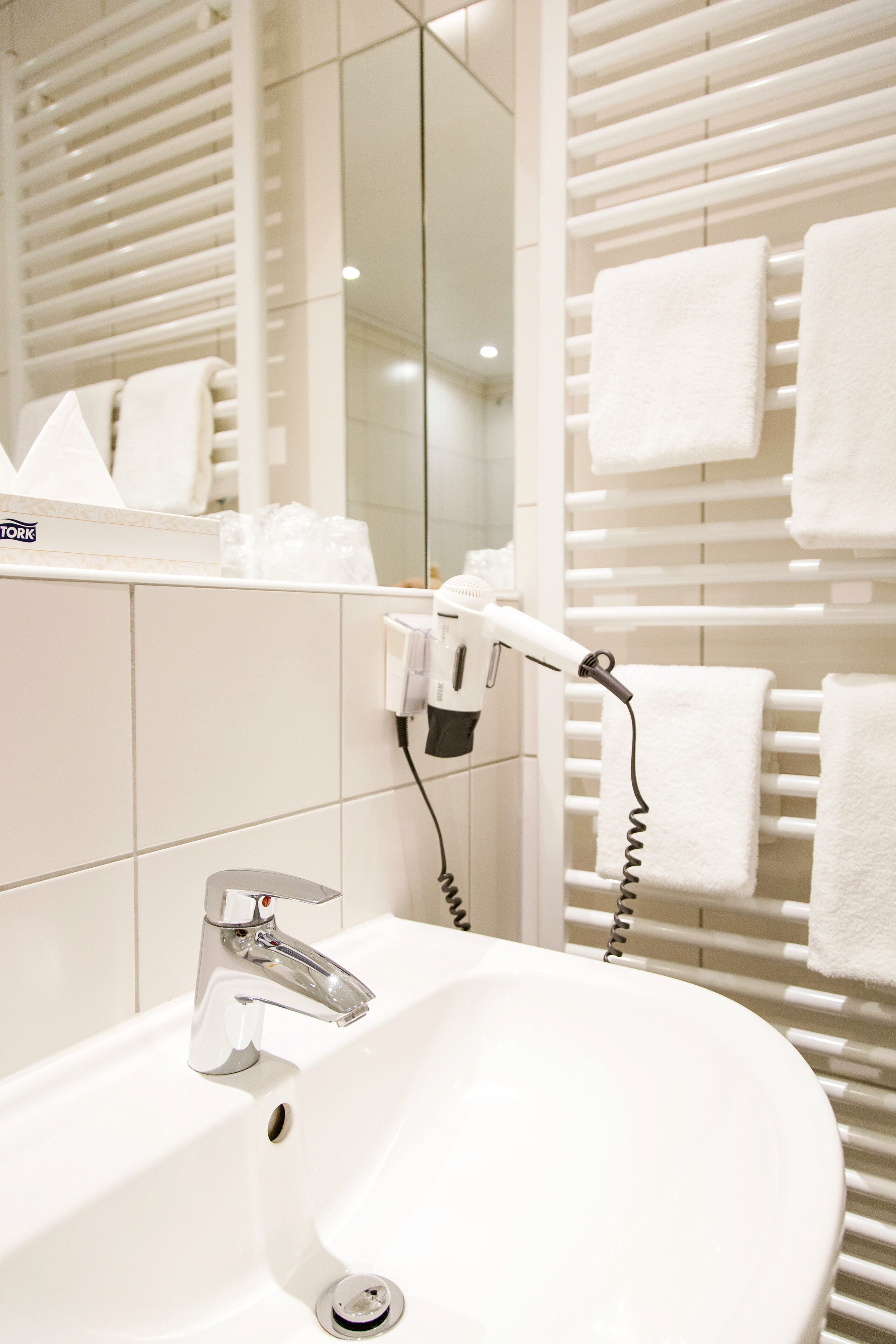 A bathroom with a white sink, a hairdryer, and a towel rack with multiple white towels.