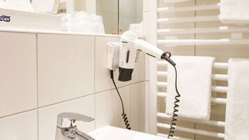 A bathroom with a white sink, a hairdryer, and a towel rack with multiple white towels.